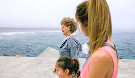 Three female generations walking by sea pier. Selective focus on senior woman in backgroundの写真素材