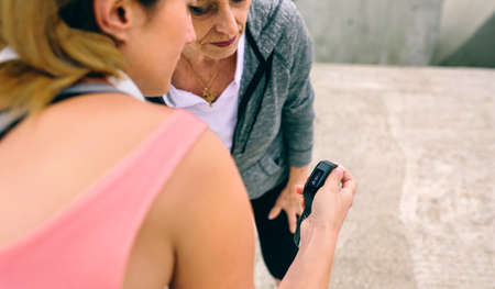 Senior woman looking smart watch with female coach outdoorsの写真素材