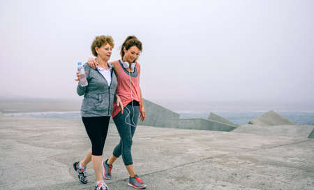 Senior woman and young woman walking outdoors by sea pierの写真素材
