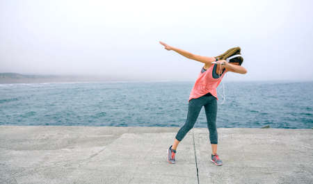 Young woman making dab dance outdoors by sea pierの写真素材