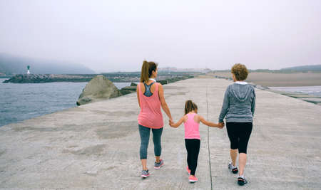 Back view of three female generations walking by sea pierの写真素材