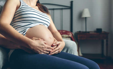 Unrecognizable pregnant woman holding her belly embraced by her husbandの写真素材