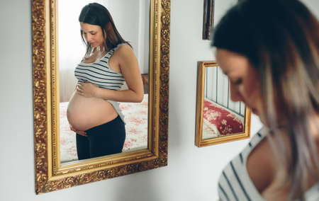 Pregnant woman looking her belly in the mirrorの写真素材