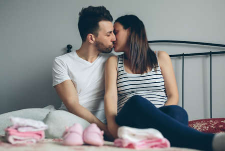 Young man kissing his pregnant wife in the bedroomの写真素材
