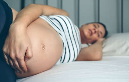 Pregnant woman sleeping and holding her bellyの写真素材