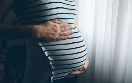 Unrecognizable pregnant woman holding her tummy in the bedroom