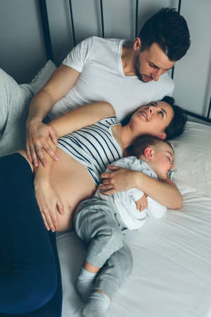 Pregnant woman sharing bed with man and little boyの写真素材