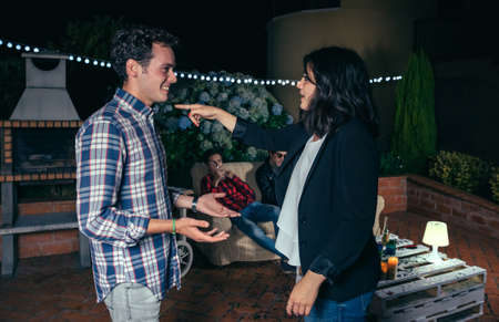 Young woman pointing with her finger to smiling man in a outdoors party with their friends in background. Friendship and celebrations concept.の写真素材