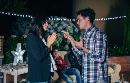Man and woman arguing in a night party outdoors with their friends on background. Couple...