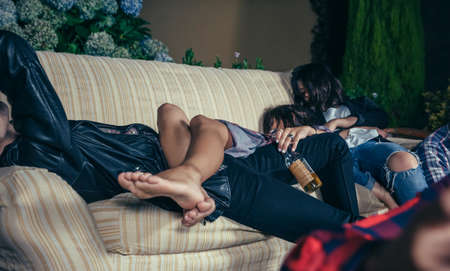 Close up of young drunk woman sleeping in a sofa over her friends after outdoors party. Fun and alcohol and drugs problems concept.の写真素材