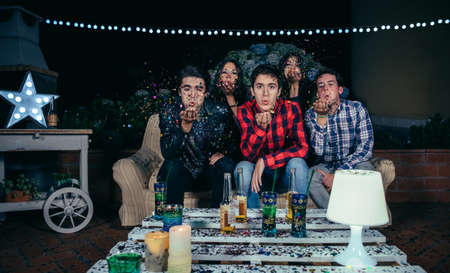 Young friends blowing colorful confetti to the camera in a outdoors party. Friendship and...