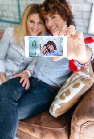Top view of couple taking selfie on a sofa in a coffee shop. Selective focus on mobile in the foregroundの写真素材