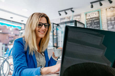 Woman drinking coffee and chatting with the laptop in a coffee shop