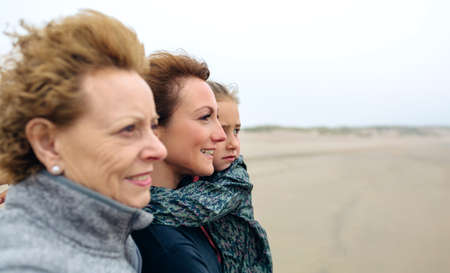 Closeup of three generations female looking at sea on the beach in autumn. Background focus on young woman and childの写真素材