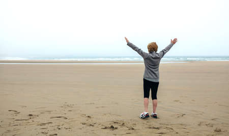 Back view of senior woman watching the sea in autumn with hands up