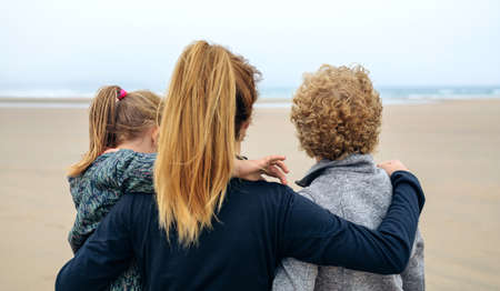 Back view of three generations female looking at sea on the beach in autumnの写真素材