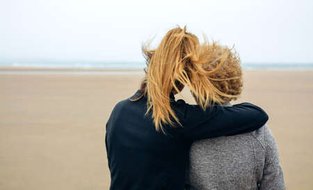 Back view of senior and young woman looking at sea on the beach in autumnの写真素材