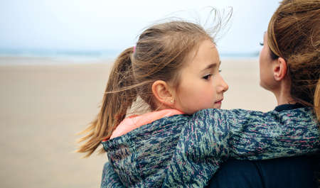 Back view of mother and daughter looking at sea on the beach in autumnの写真素材