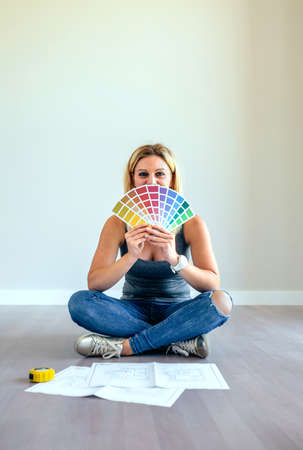 Young woman with color chart sitting in a empty living room