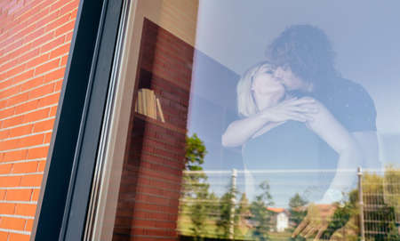 Couple kissing behind the window of their new house
