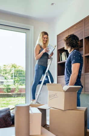 Couple unpacking moving boxes and placing books on the shelf