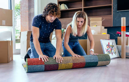 Couple unpacking moving boxes and unrolling the carpetの写真素材