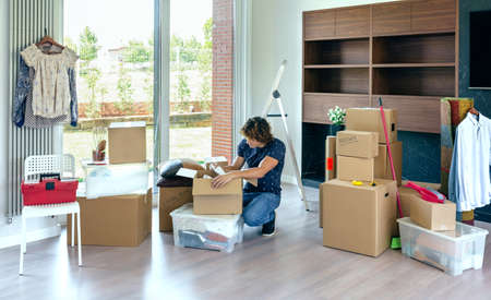 Young man unpacking moving boxes in living room