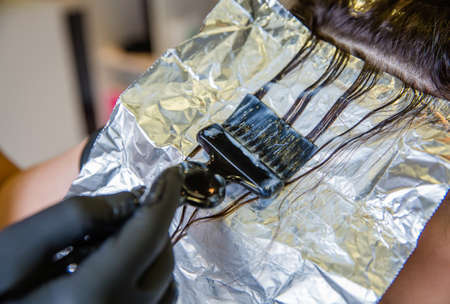 Closeup of hairdresser hands applying hair dye to beautiful young womanの写真素材