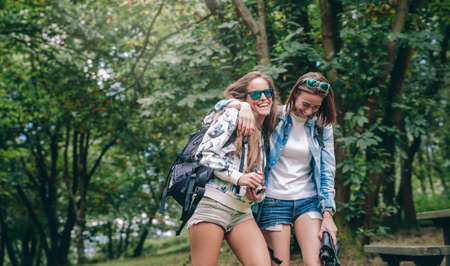 Portrait of women friends with backpacks laughing while walking in the forestの写真素材