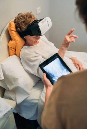 Older patient using virtual reality glasses to see her spine while female doctor explainsの写真素材