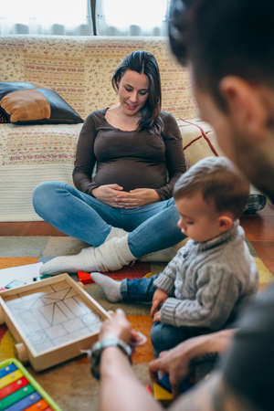 Young father playing with his toddler a wooden game building in the living room while the pregnant...
