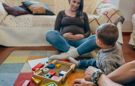 Young father playing with his toddler son a wooden game building in the living room while the mother is looking at themの写真素材