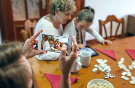 Grandmother and granddaughter play a game on the tablet while the mother takes a photo with the smartphone. Selective focus on smartphone in foregroundの写真素材