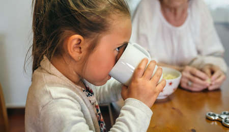 Little girl drinking a cup of milk with her grandmotherの写真素材