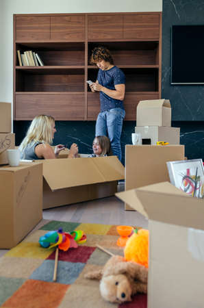 Mother and son playing sitting inside a moving box while the father looks at the mobileの写真素材
