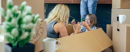 Mother and son playing sitting inside a moving box while the father looks at the mobile