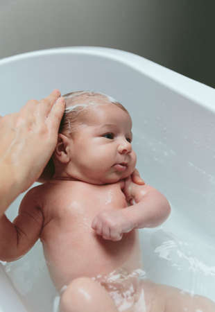 Portrait of relaxed newborn girl in the bathtub with her mother washing her hairの写真素材