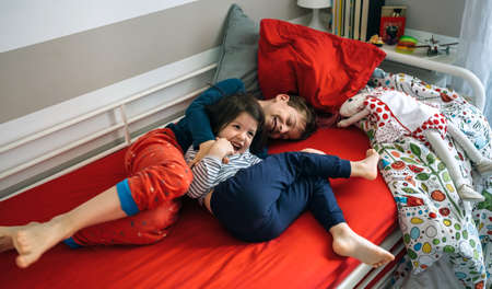 Brother and sister tickling and laughing while lying on the bed