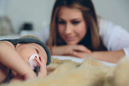 Newborn baby girl sleeping lying on a blanket on the bed while her mother looks at her. Selective focus on baby in foregroundの写真素材