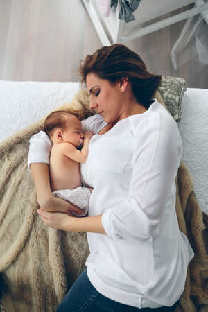 Top view of young mother hugging her newborn baby girl lying on the bed