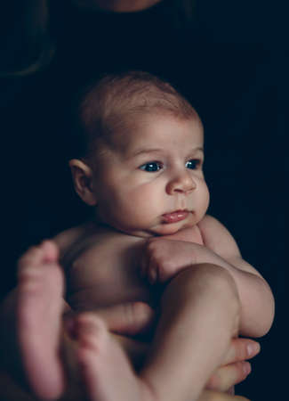 Nude baby girl posing in her mother's arms on black background