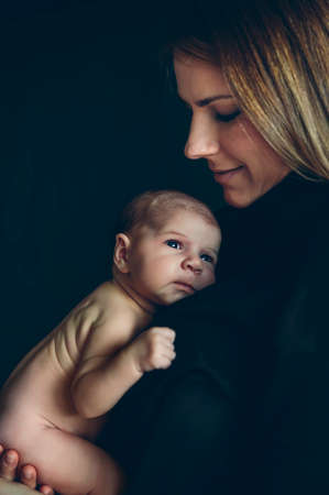 Nude baby girl posing in her mother's arms on black backgroundの写真素材