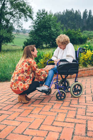 Affectionate young woman talking to elderly woman in a wheelchair in the garden