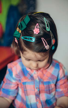 Protrait of cute baby girl head with a lot of hair clips playing over a wooden floor at home. Selective focus on head.の写真素材