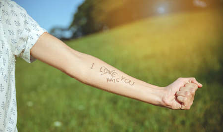 Closeup of male arm with the text -I hate you- and word -love- crossed out in the skin over a sunny nature backgroundの写真素材