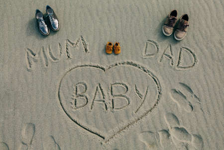Mum, dad and baby written on the sand of the beach next to their shoesの写真素材