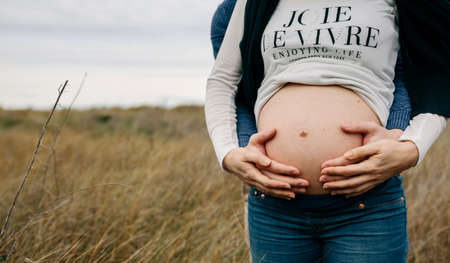 Unrecognizable pregnant with her partner hugging her and holding her naked bellyの写真素材