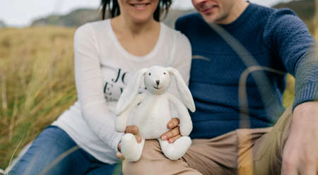 Happy couple showing a stuffed bunny announcing their pregnancyの写真素材