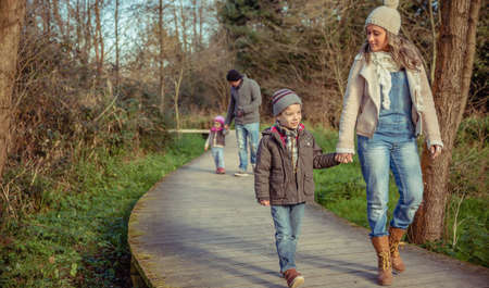Happy family walking together holding hands over a wooden pathway into the forestの写真素材
