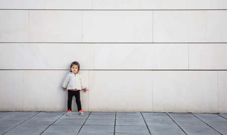 Little girl with sportive look posing in front of a modern white stone wallの写真素材